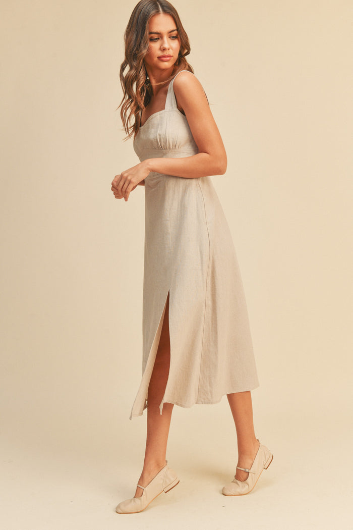 woman wearing a beige linen midi dress with a side slit and matching flat shoes