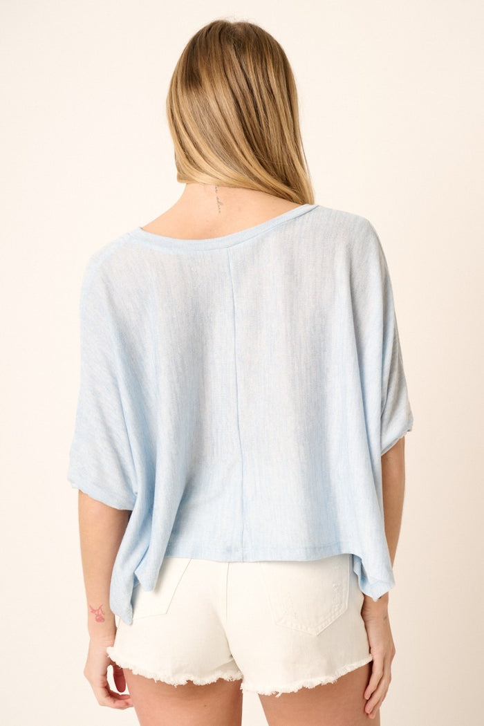 Back view of a woman wearing a light blue short sleeve knit top and white denim shorts