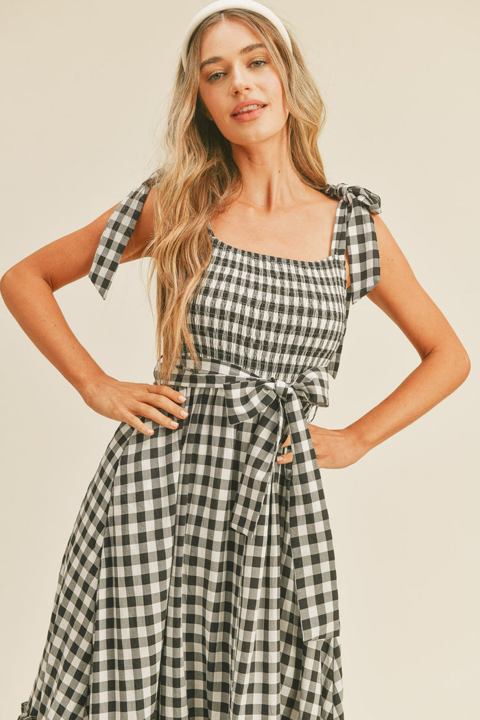 Woman wearing a black and white gingham midi dress with tie straps and a matching waist bow