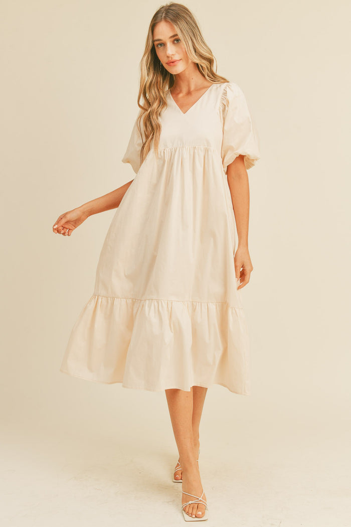 woman wearing a cream puff sleeve midi babydoll dress with a v-neckline and ruffled hem