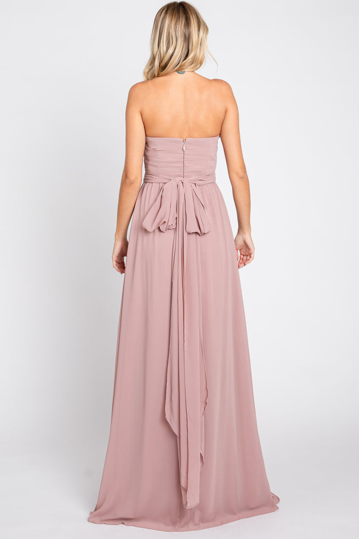 woman wearing a blush strapless maxi dress with a tied bow detail at the back