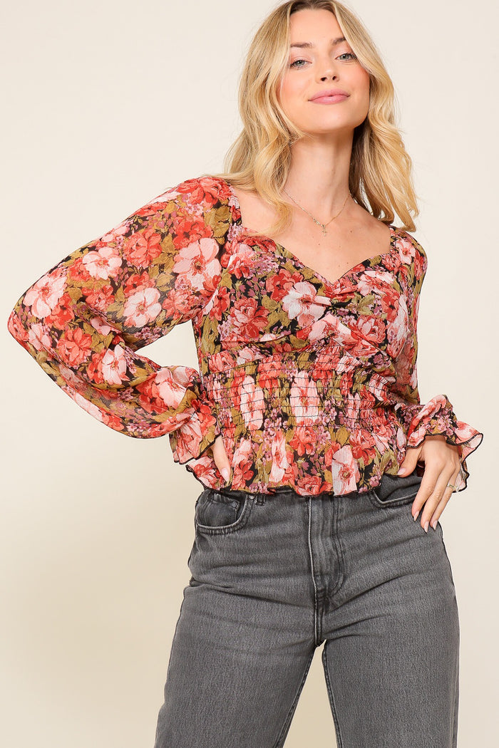 woman wearing a floral long sleeve blouse with a smocked bodice and ruffled cuffs paired with high-waisted jeans